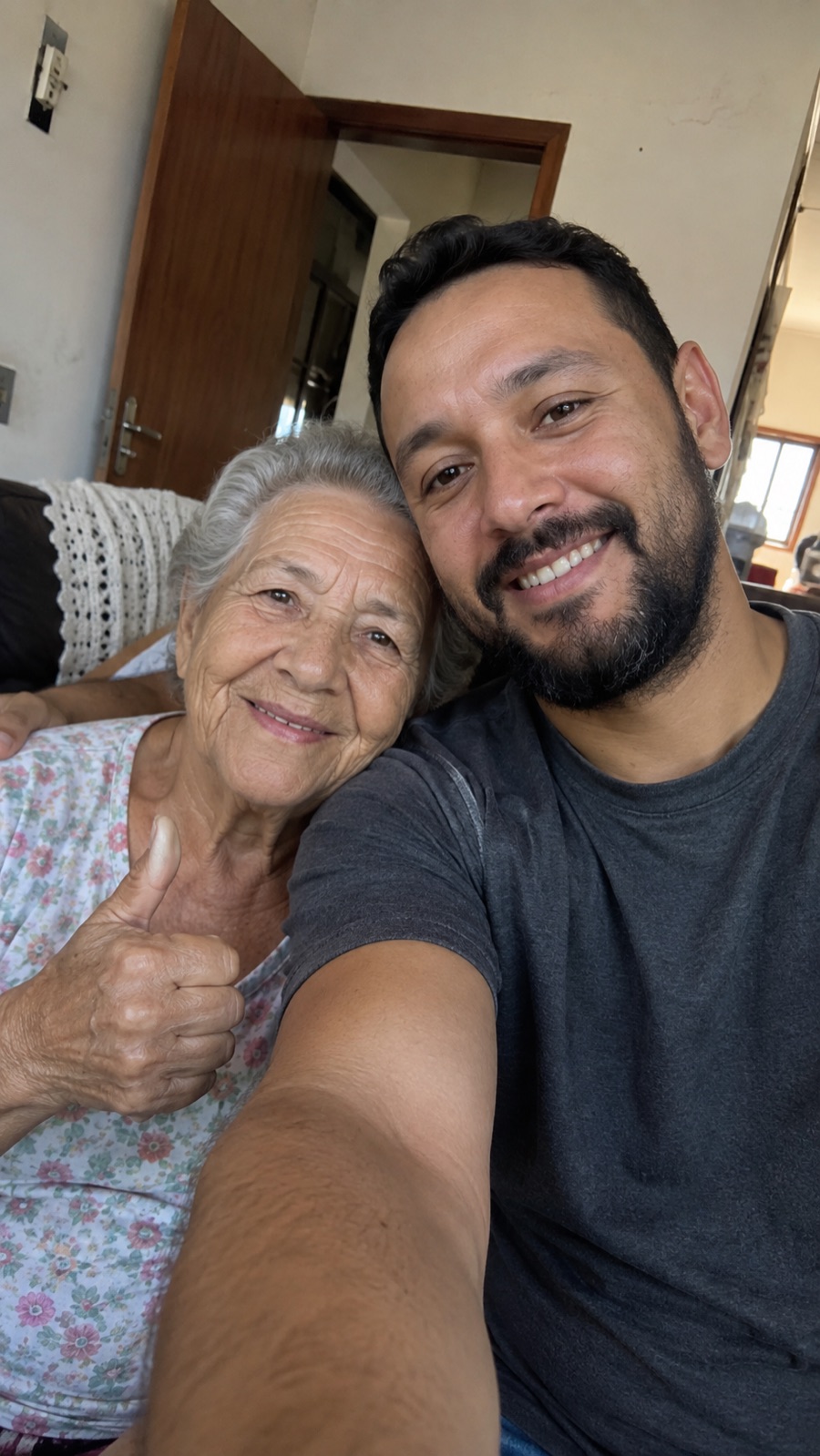 Filho adulto abraçado com a mãe idosa, os dois sorrindo em casa